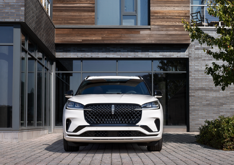 A white 2025 Lincoln Aviator® SUV is shown parked outside a modern building with gray brick and wood accents. | Bluebonnet Motors Lincoln in New Braunfels TX