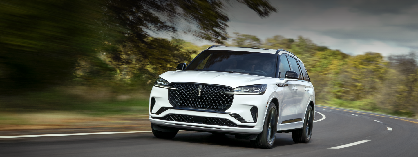A white 2025 Lincoln Aviator® SUV is being driven down a road lined with trees. | Bluebonnet Motors Lincoln in New Braunfels TX