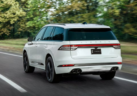 A white 2026 Lincoln Aviator® SUV is being driven away down a road lined with colorful trees. | Bluebonnet Motors Lincoln in New Braunfels TX
