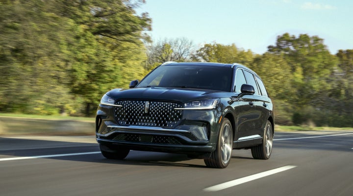 A 2026 Lincoln Black Label™ Aviator® SUV is being driven down a road lined with trees. | Bluebonnet Motors Lincoln in New Braunfels TX