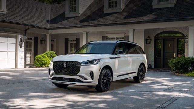 A white 2026 Lincoln Aviator® SUV is parked in the driveway of a luxury home. | Bluebonnet Motors Lincoln in New Braunfels TX