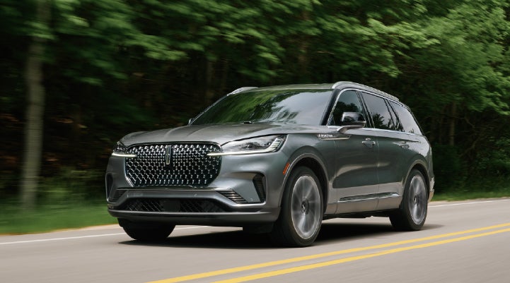 A 2027 Lincoln Aviator® SUV is being driven down a road lined with trees. | Bluebonnet Motors Lincoln in New Braunfels TX
